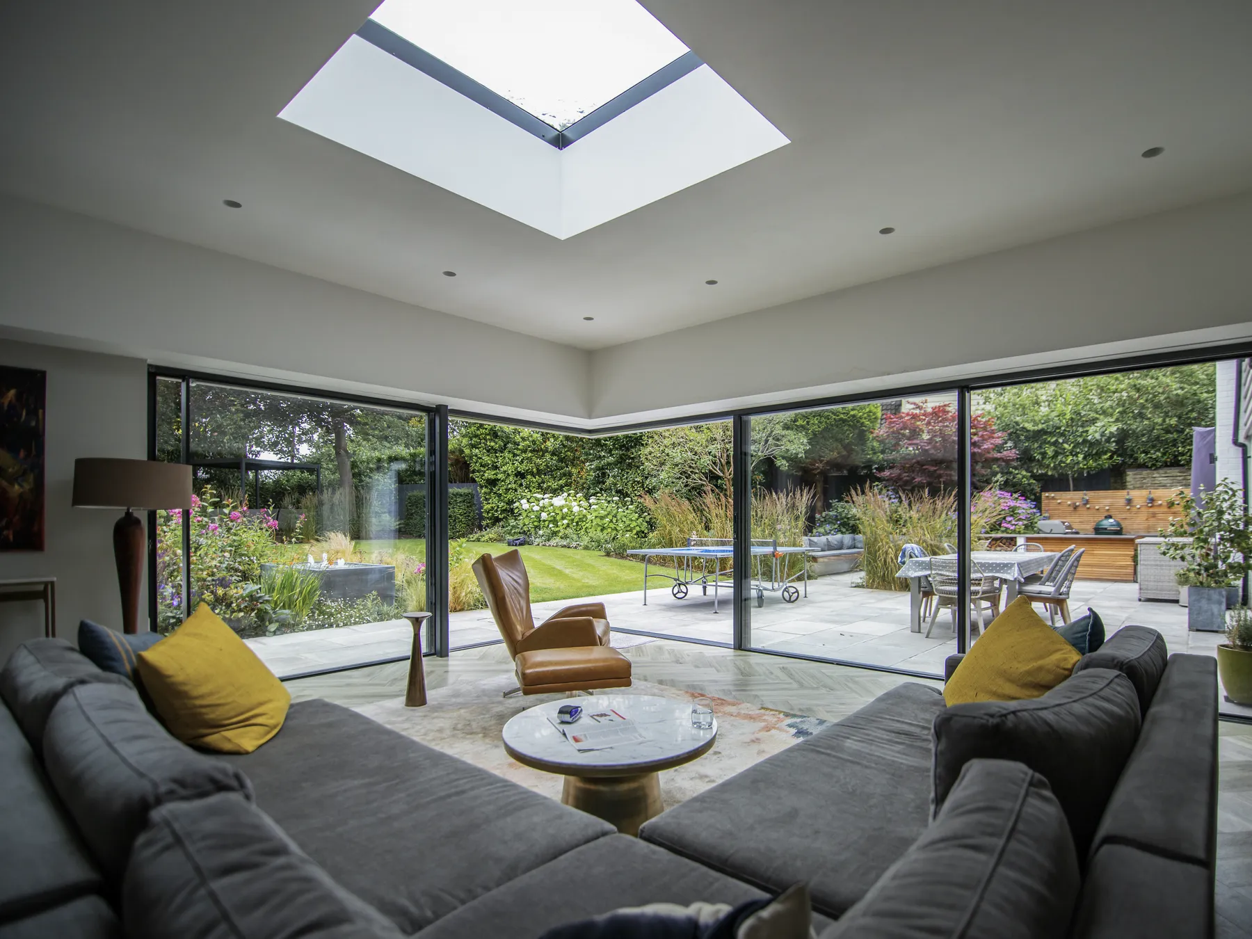 Living room under a rooflight, framed by slim sliding glass